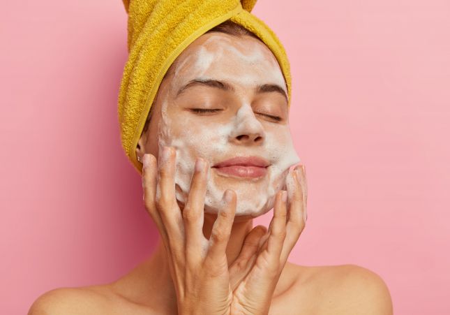 relaxed pretty woman cares about her appearance washes face with pleasant facial gel or soap removes all pores keeps eyes shut from pleasure gets hygienic treatments